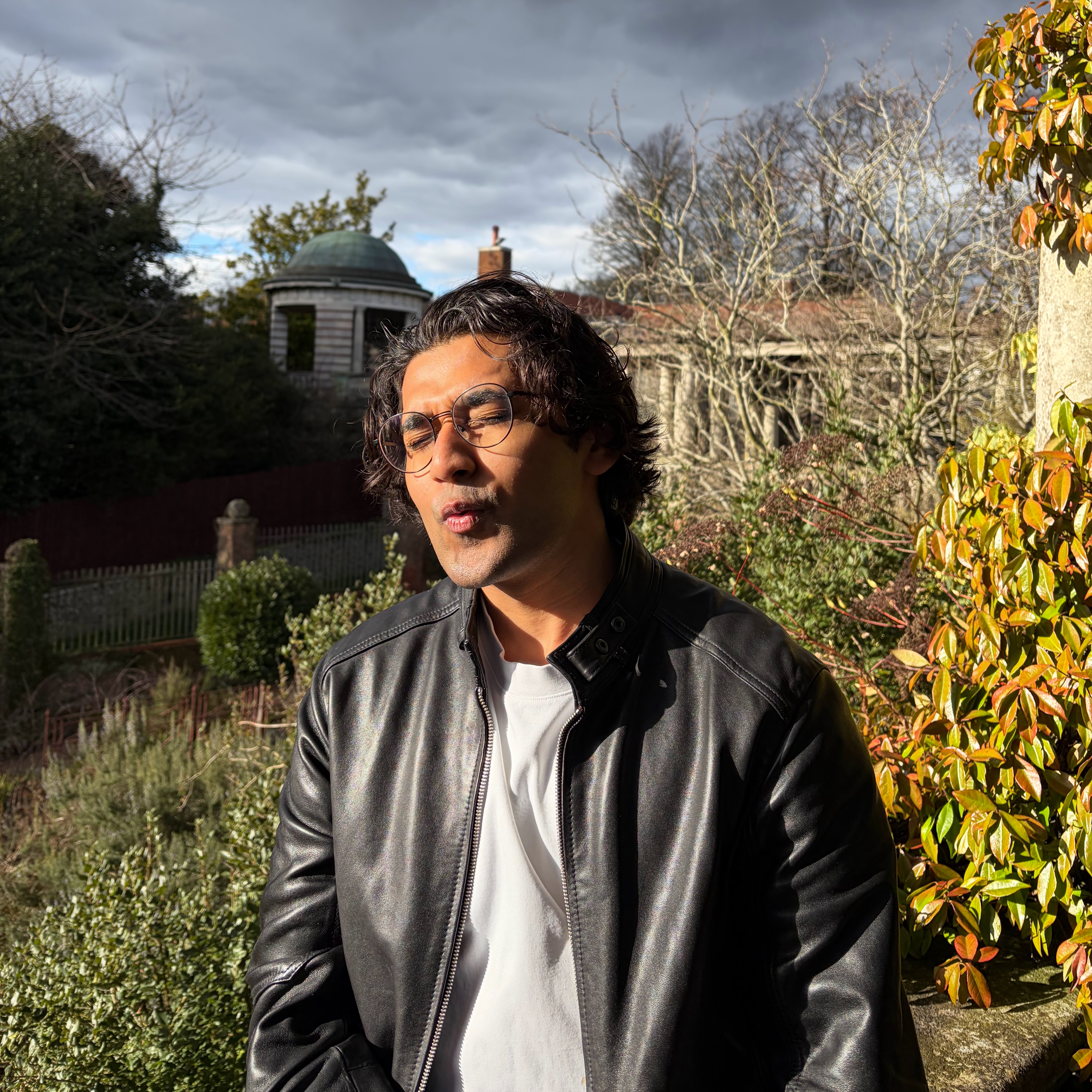 Aryan sitting in a garden with eyes closed, sun on his face