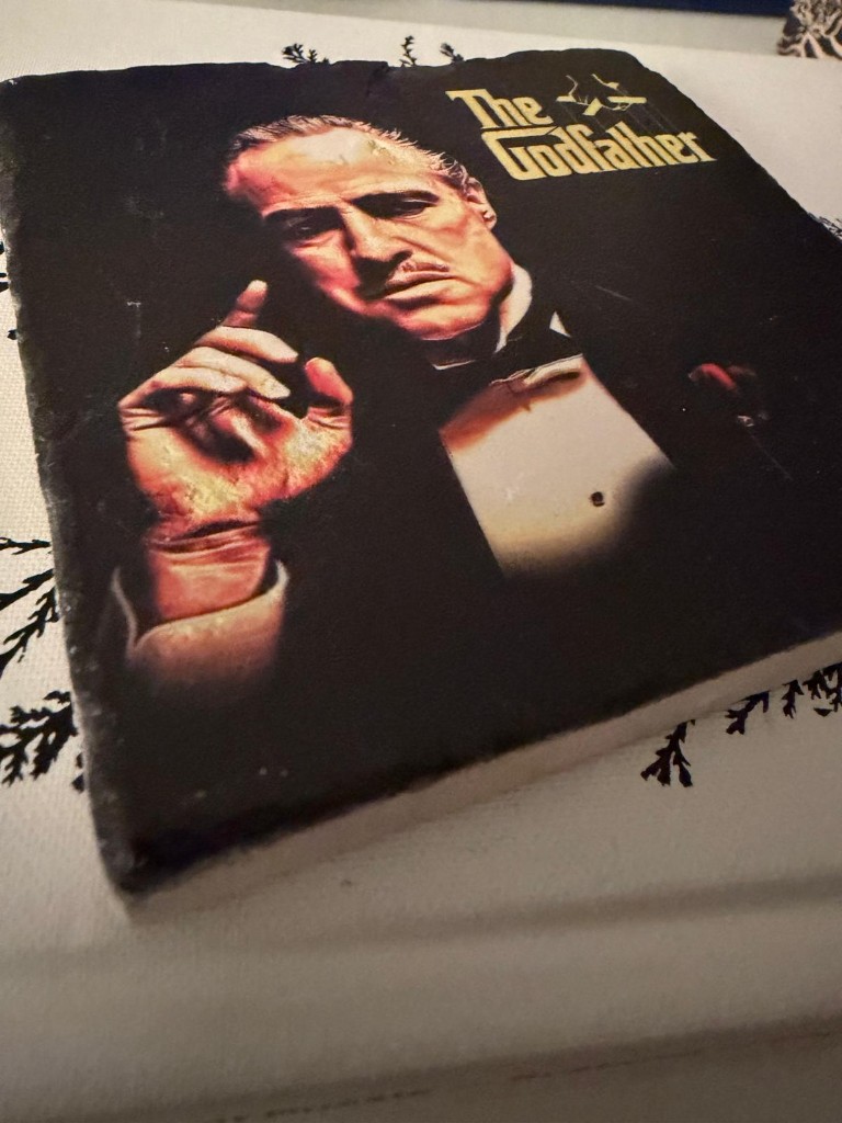 The Godfather poster on a square slate coaster: Don Vito Corleone in a tuxedo, hand raised, gold title lettering